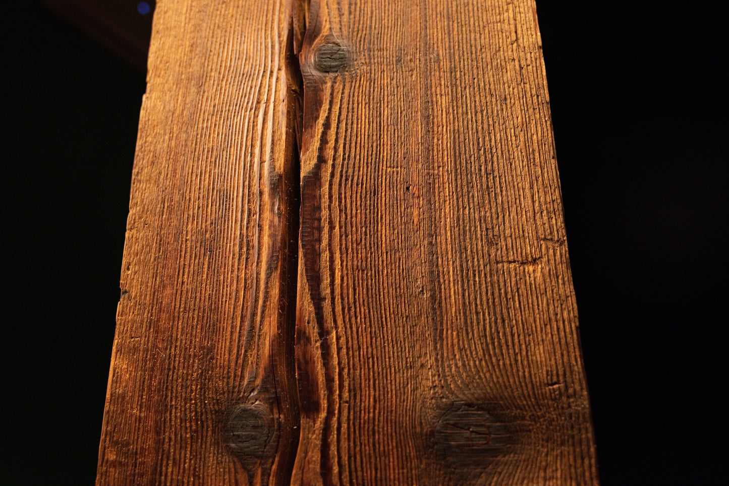 Close perspective highlighting a dark organic knot embedded within the sweeping side grain of an investment-grade beam.  