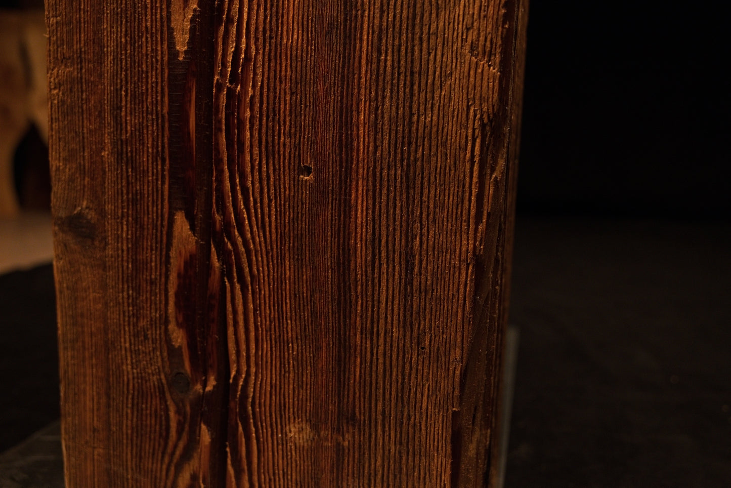 Close detail of an authentic dark knot and deep vertical channeling along the sharp corner of a biophilic architectural centerpiece.  