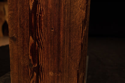 Close detail of an authentic dark knot and deep vertical channeling along the sharp corner of a biophilic architectural centerpiece.  