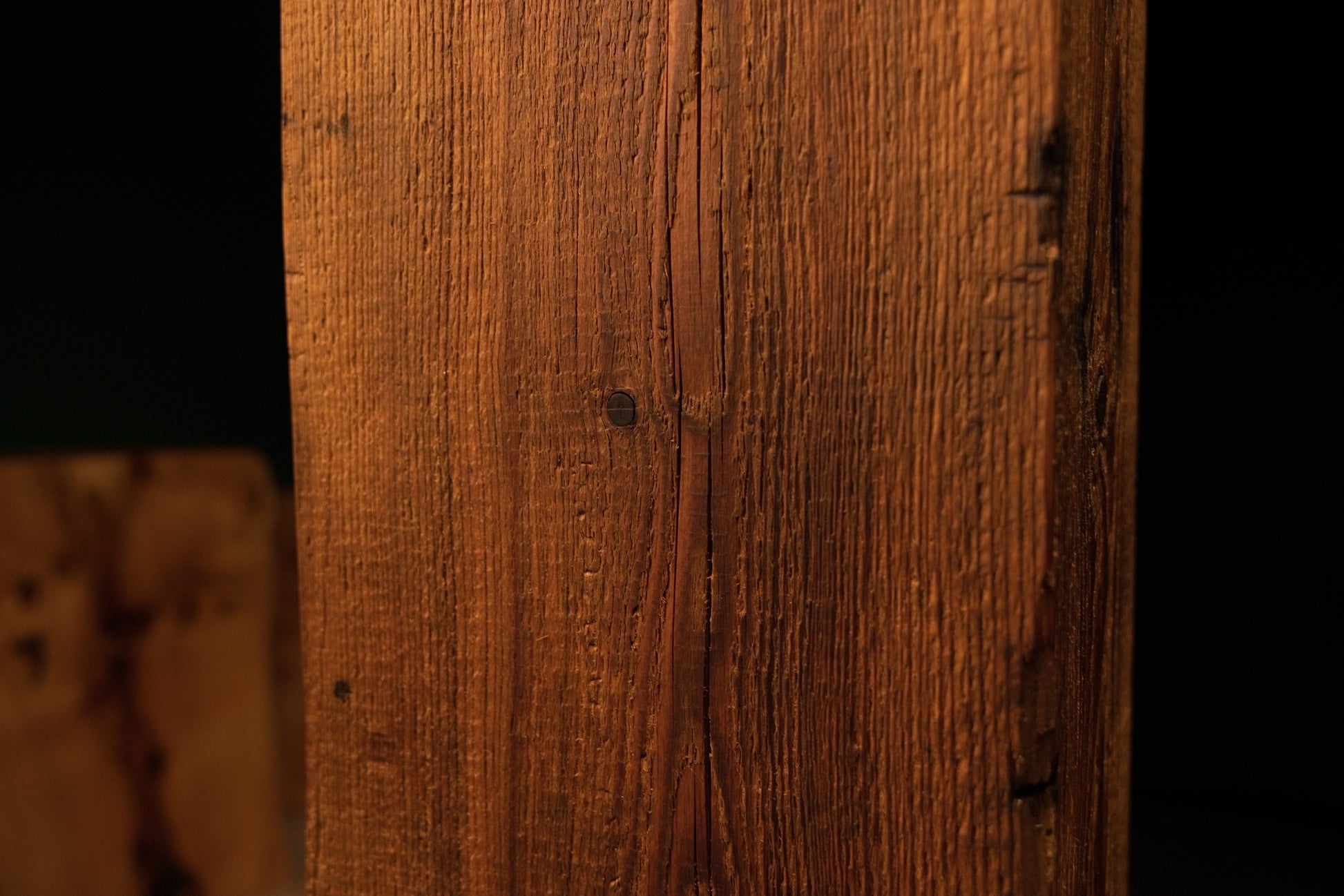 Detailed focus on wavy vertical fibers swirling dynamically around a dark organic knot on a museum-quality structural timber.  