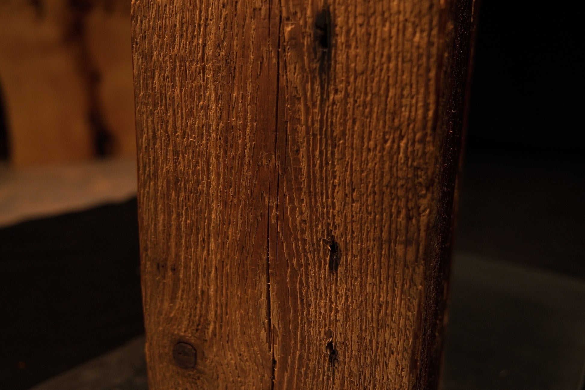 Close detail of a historic dark nail void embedded in the tight vertical golden grain of a museum-quality structural timber.  