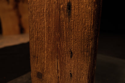 Close detail of a historic dark nail void embedded in the tight vertical golden grain of a museum-quality structural timber.  