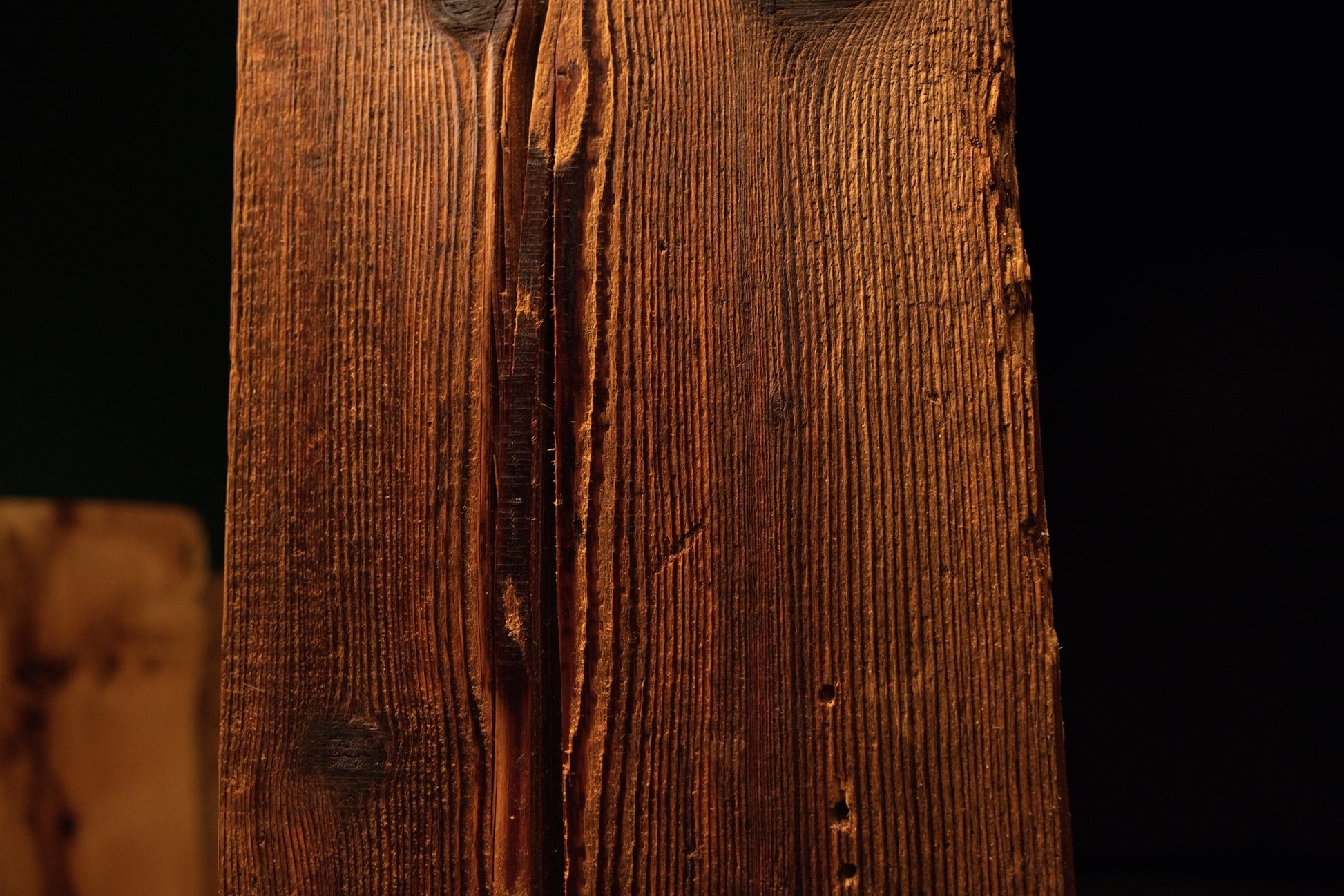 Macro view of a jagged natural fissure casting dark shadows across the deeply furrowed face of a climate-stable timber block.  