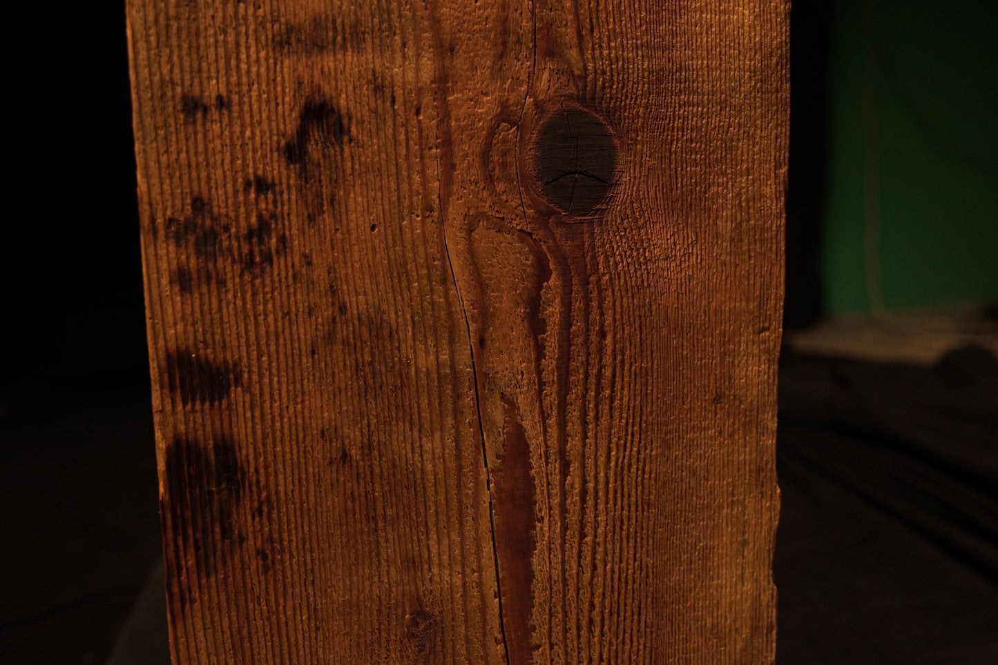 Close detail of a dark organic knot cluster and scattered surface discoloration running down the face of a structural log. 