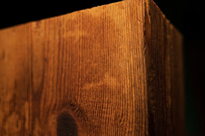 Extreme macro of a dark organic knot positioned near the upper corner of a floor-heating safe architectural wood column. 