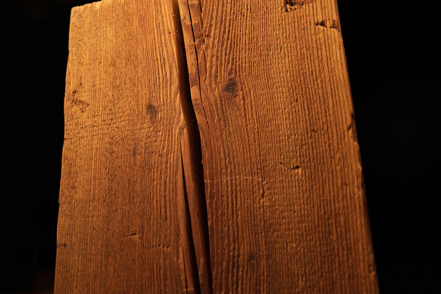Close-up of a dark vertical wood split running centrally down the textured face of a beam. 