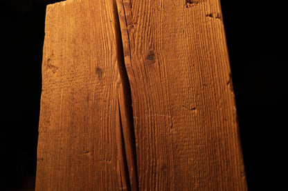 Close-up of a dark vertical wood split running centrally down the textured face of a beam. 