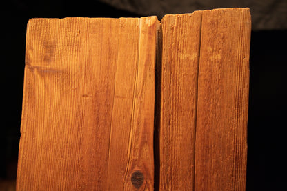 Macro detail of a narrow vertical surface split intersecting a dark organic knot near the upper face of a wooden beam. 