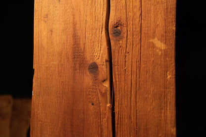 Detailed macro of a winding central surface split flanked by two dark biological wood knots on a structural salvage element. 