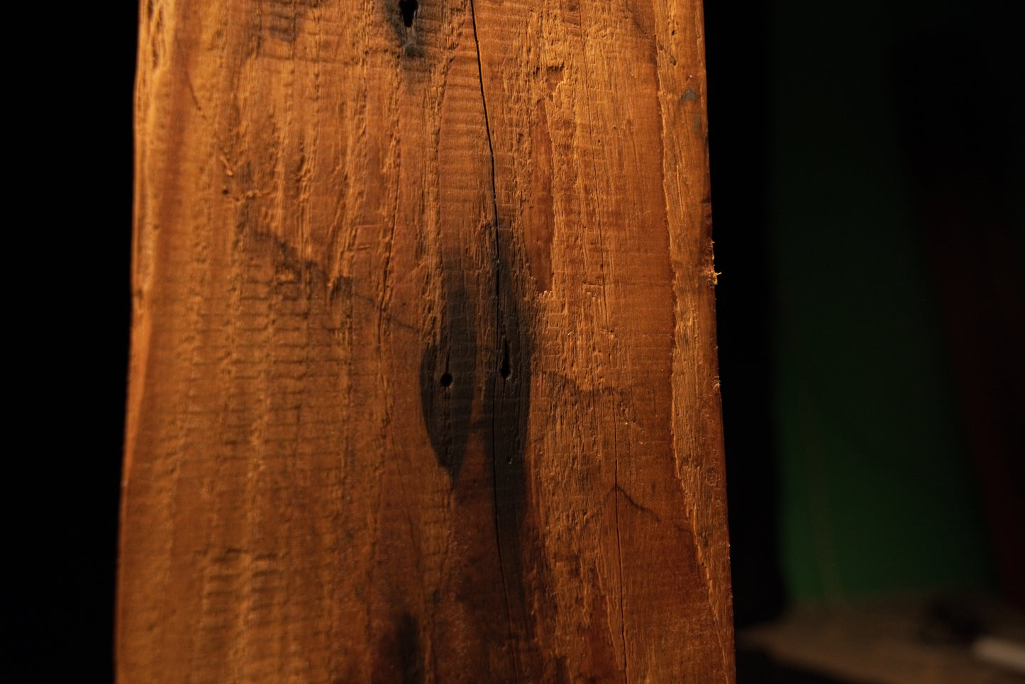 Extreme close-up of a dark organic inclusion nestled within deeply furrowed vertical wood grain on a commercial timber piece. 