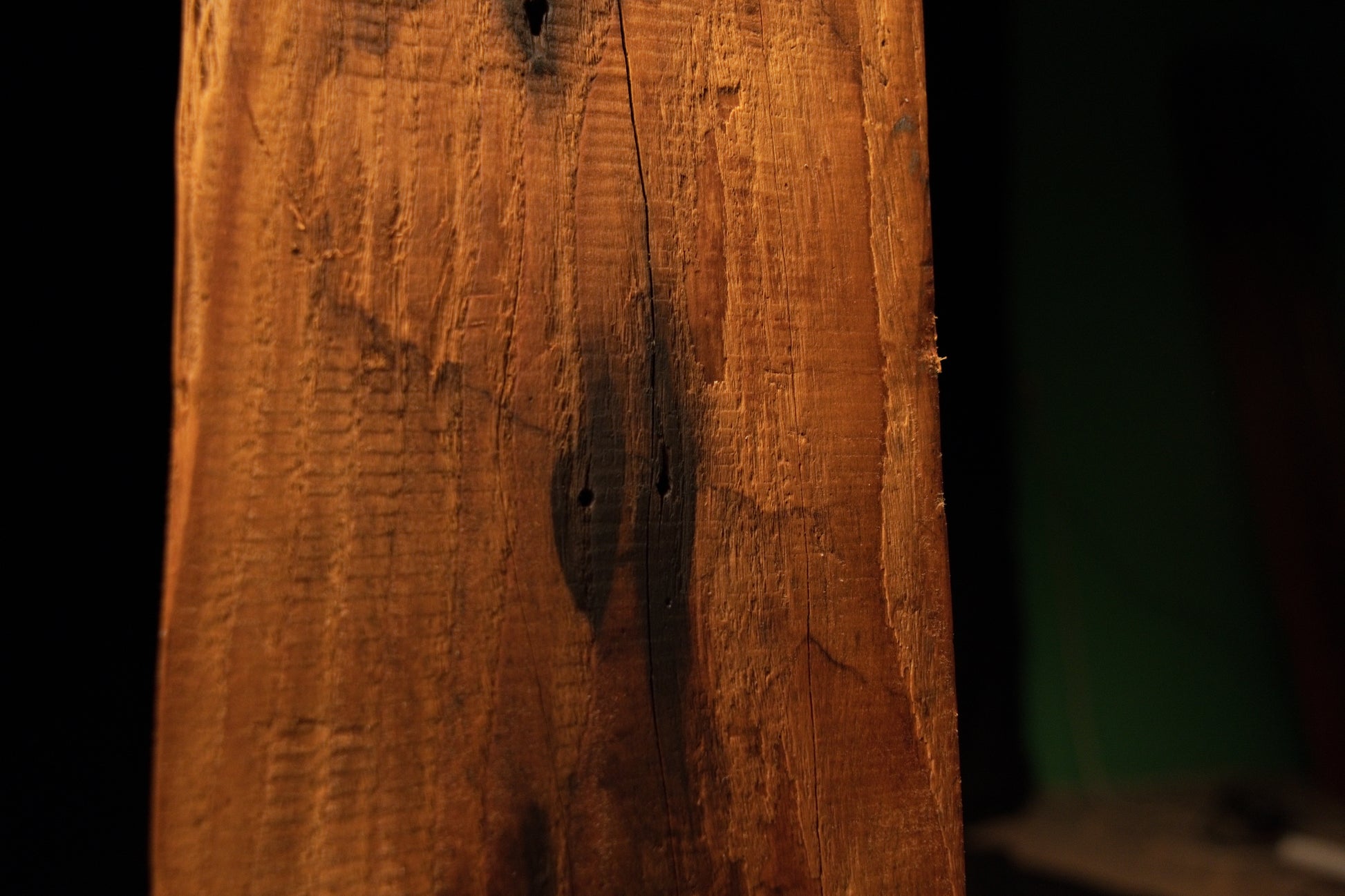 Extreme close-up of a dark organic inclusion nestled within deeply furrowed vertical wood grain on a commercial timber piece. 
