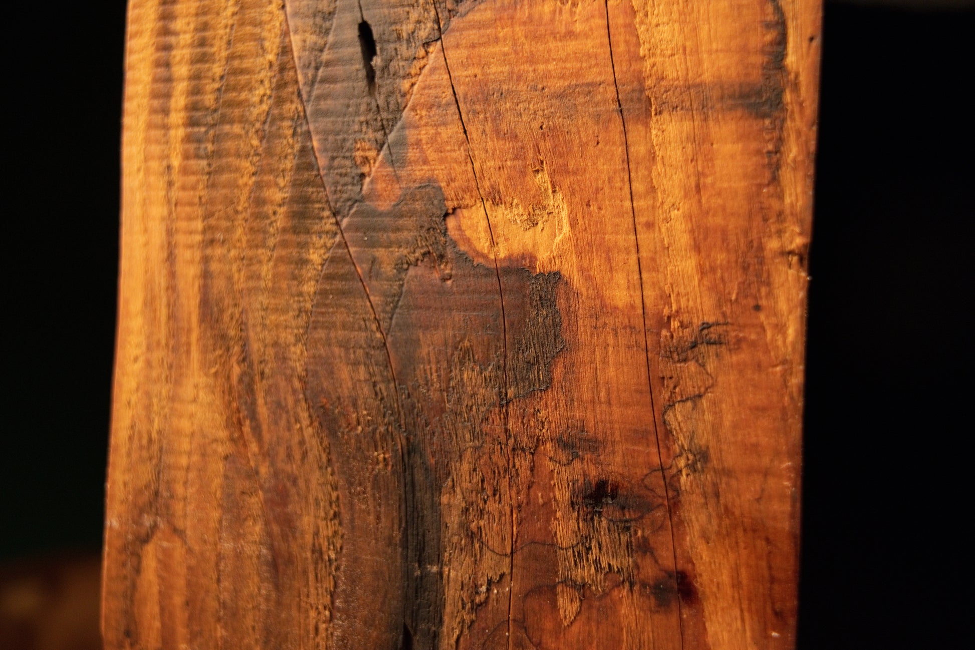 Macro view of a dark oxidation patch and micro-cracks spreading across the golden vertical fibers of a structural timber block. 