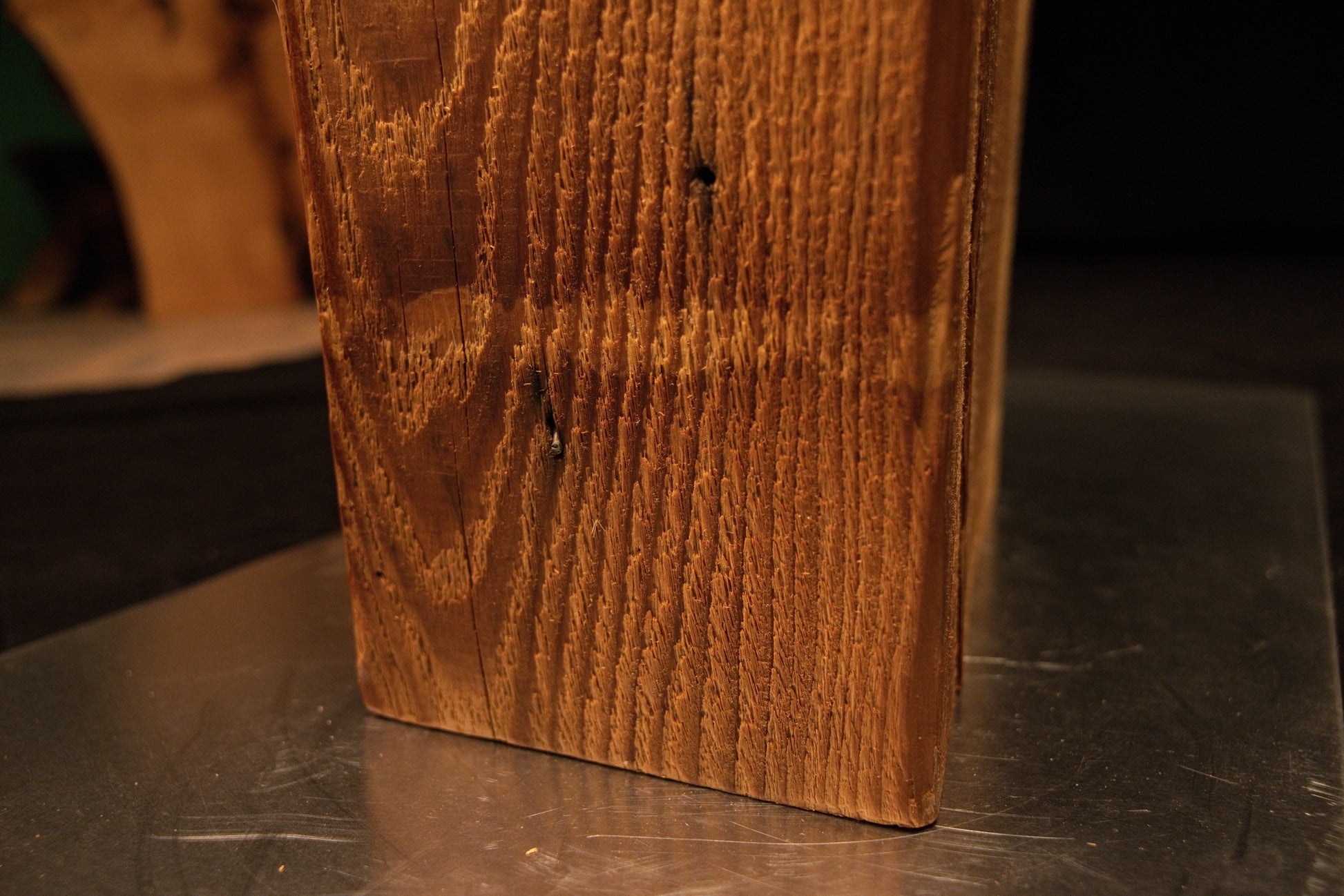 Detailed close perspective of the bottom corner where vertical grain lines meet the flat horizontal base cut resting on the metal plate. 