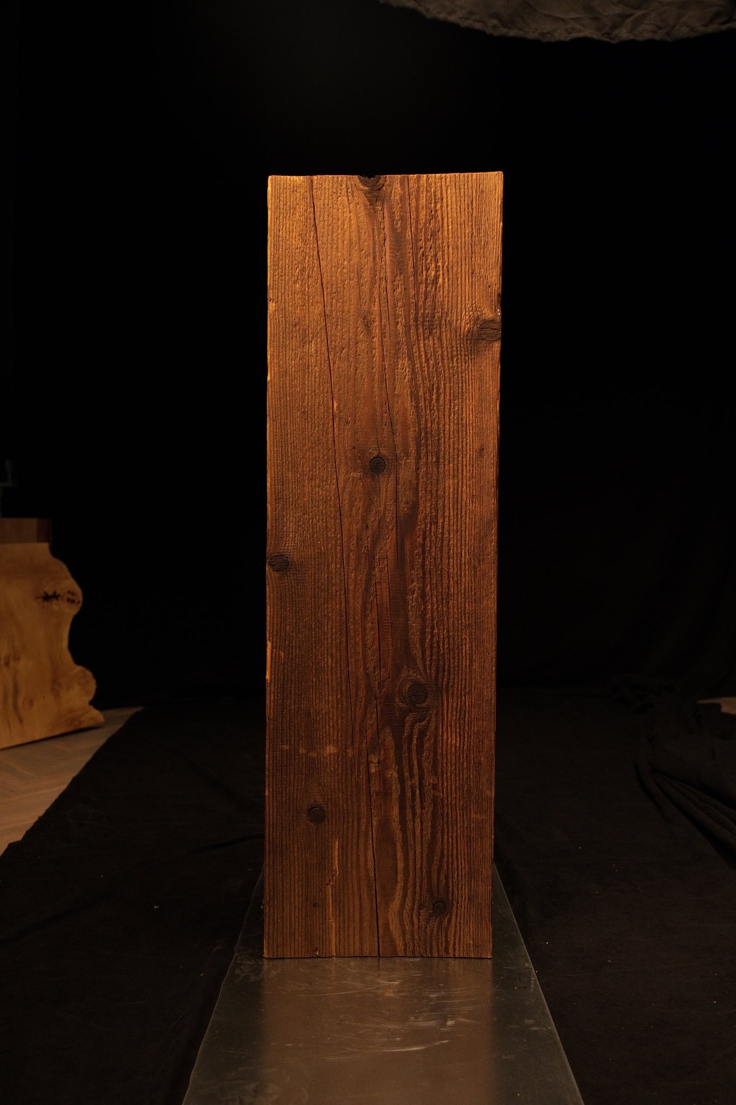 Full standing view of a vertical wooden beam featuring dense linear grain and scattered dark knots against a dark background. 