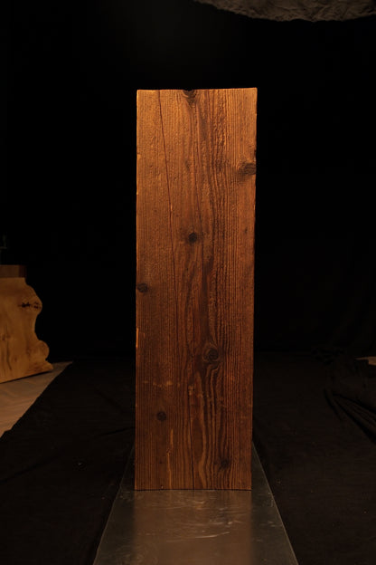Full standing view of a vertical wooden beam featuring dense linear grain and scattered dark knots against a dark background. 