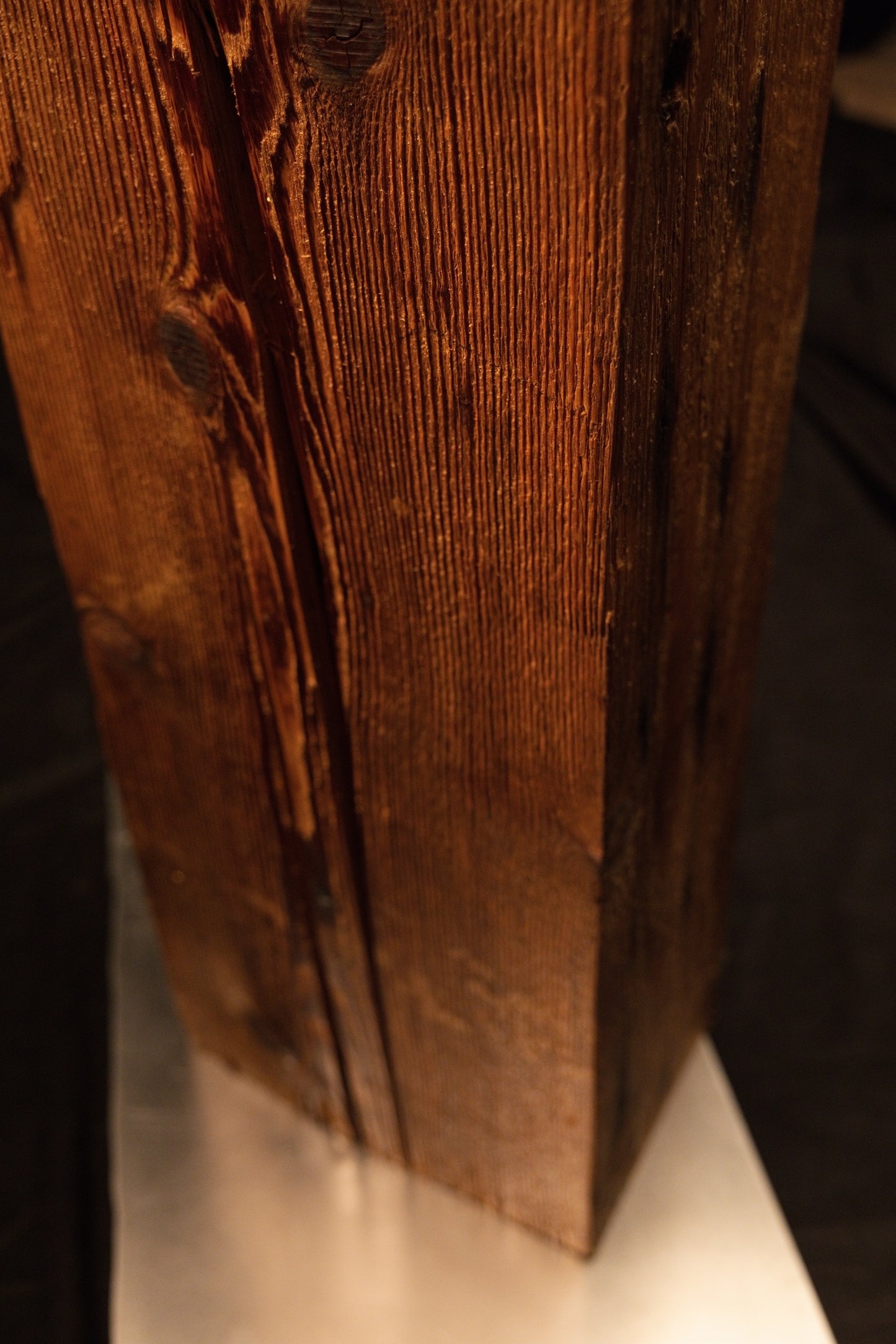 Low angle perspective capturing the lower section of a vertical wooden post with linear grain meeting a metal base. 