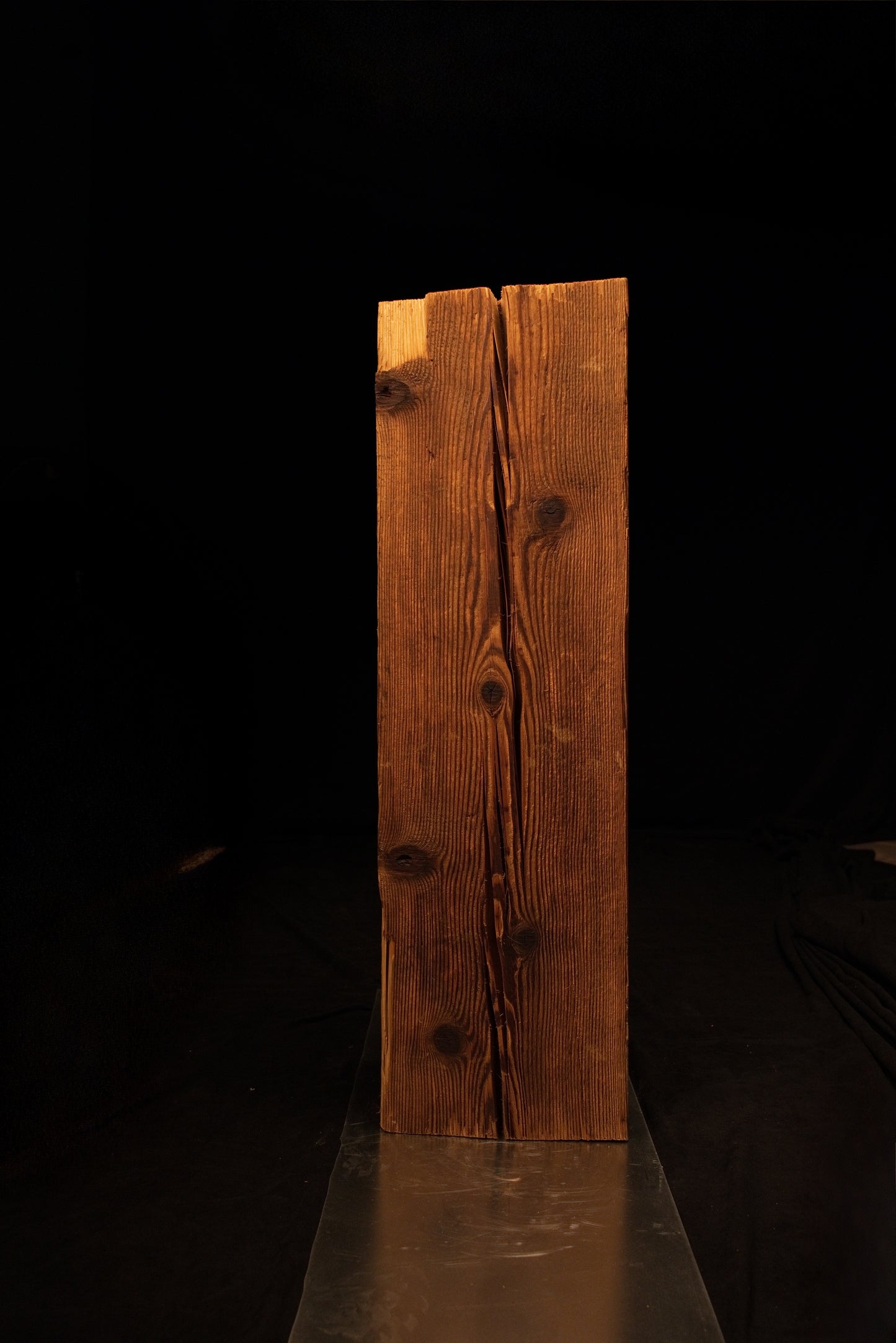 Angled elevation view of a rectangular wooden column showing a long vertical split and scattered dark knots. 