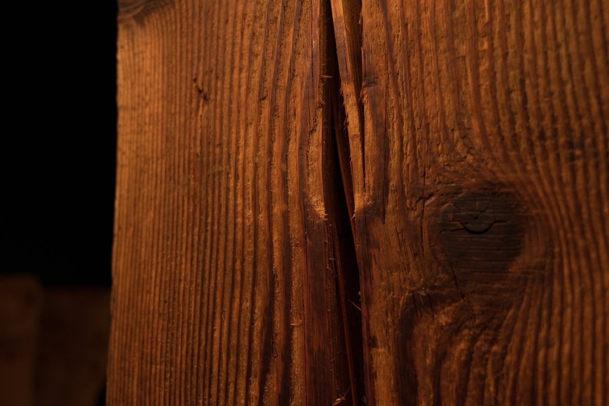 Macro photograph of a side surface split running adjacent to a dark circular wood knot on the structural beam. 