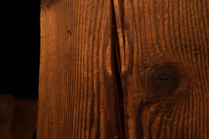 Macro photograph of a side surface split running adjacent to a dark circular wood knot on the structural beam. 