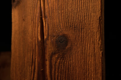 Macro view focusing on a single dark round knot positioned centrally on the vertically-grained wooden column. 