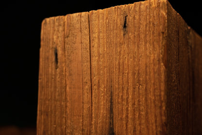 Close-up of the upper corner section on a timber post displaying linear grain and small dark pinholes near the edge. 