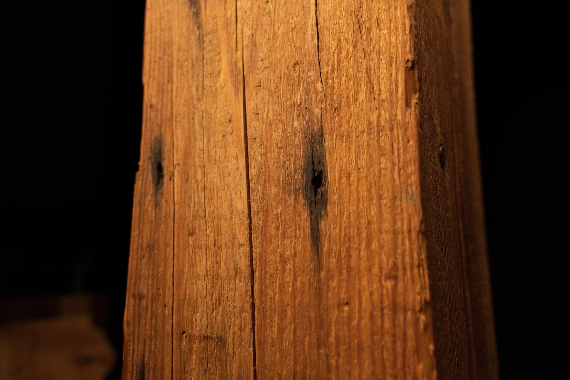 Detailed view of the beam face showing dark circular stain spots and pinholes scattered along a vertical fracture. 