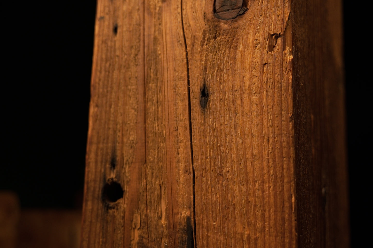 Detailed macro view of a deep circular hole and several smaller pinholes on the weathered face of the wooden beam. 