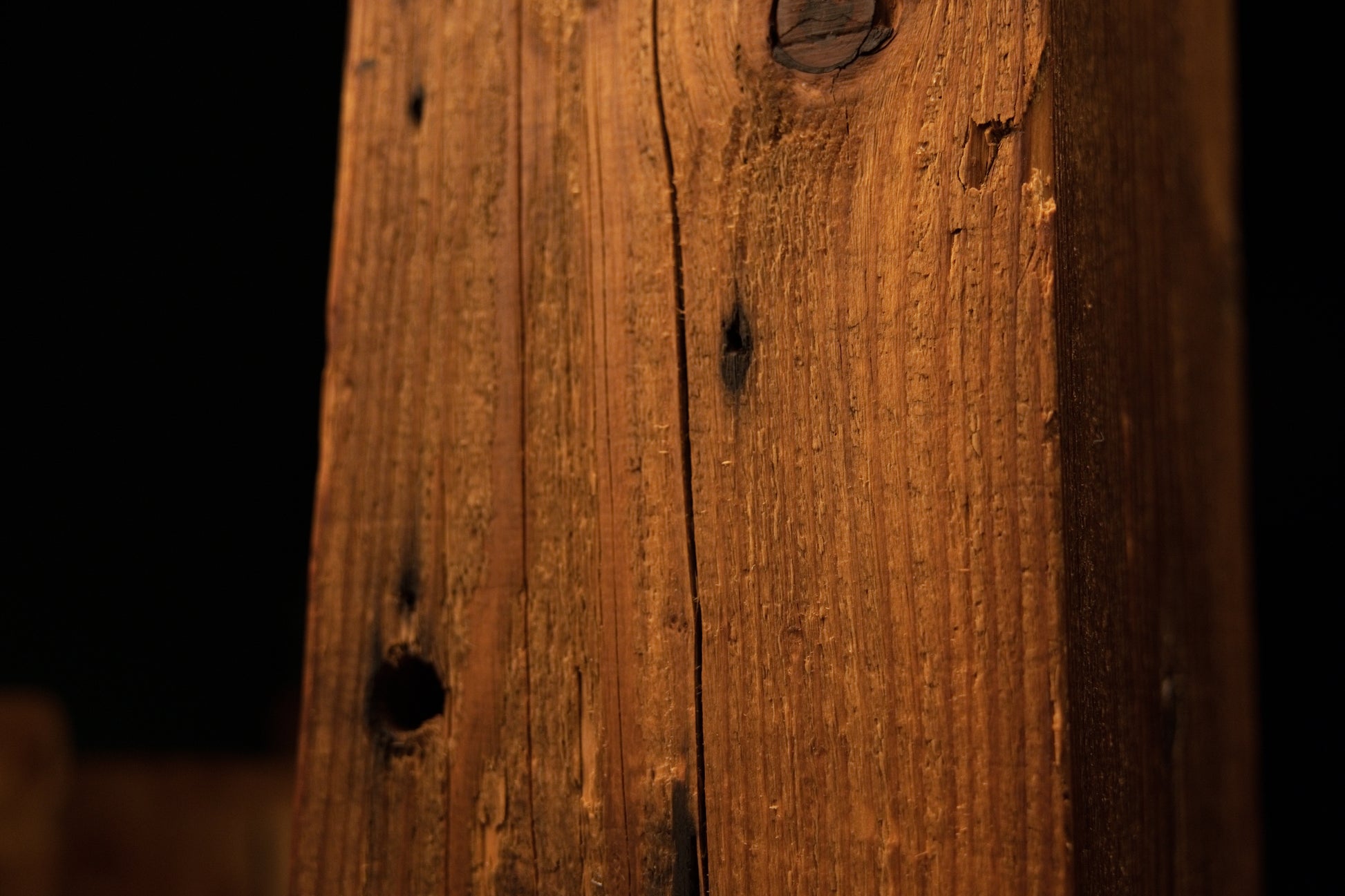 Detailed macro view of a deep circular hole and several smaller pinholes on the weathered face of the wooden beam. 