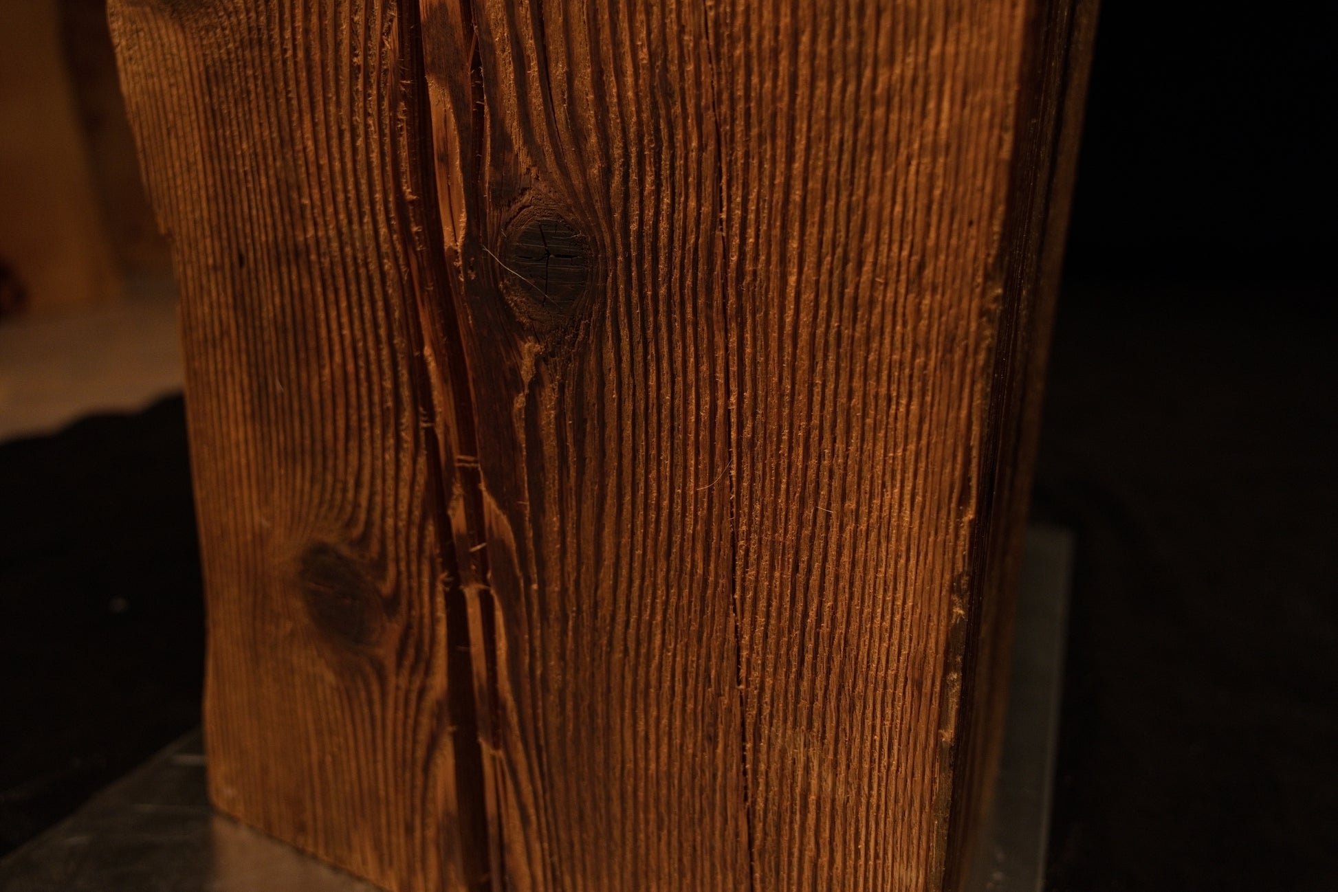 Detailed close-up of a fine vertical fracture line running alongside a dark embedded wood knot on the beam face. 
