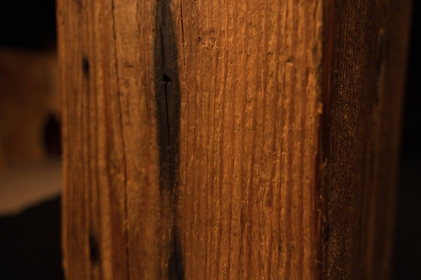 Macro photograph of straight vertical grain lines and subtle surface variations on the face of the wooden beam. 