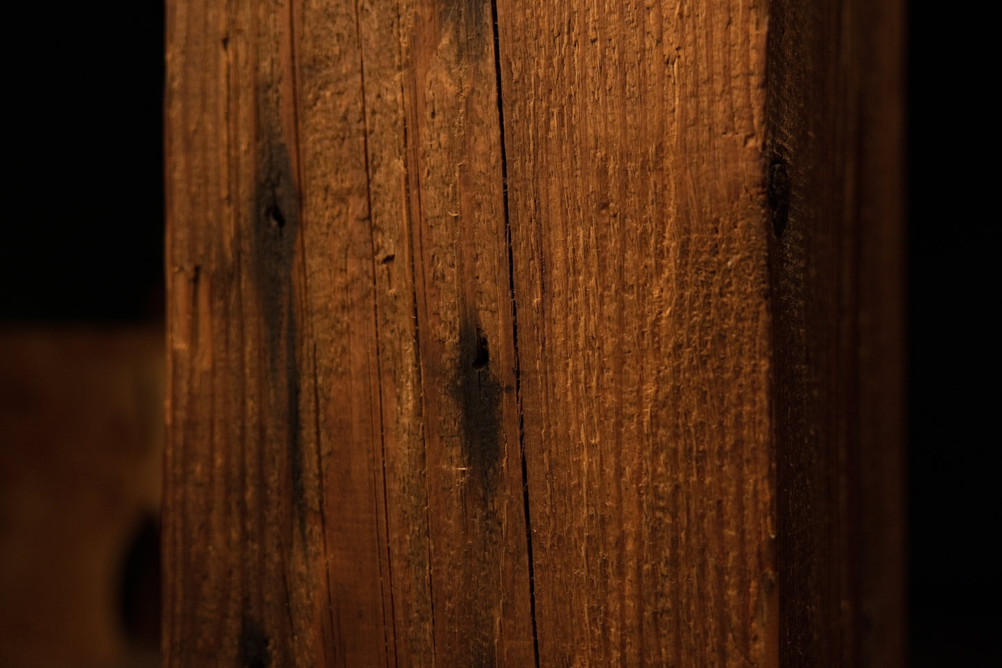 Macro photograph capturing the lower vertical corner edge and fine linear grain textures of the wooden column. 