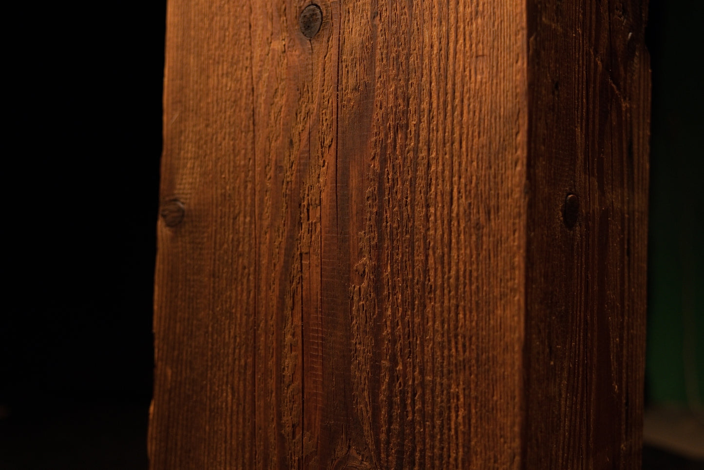 Macro perspective of uniform vertical grain lines and a small dark wood knot on the side of the structural post. 