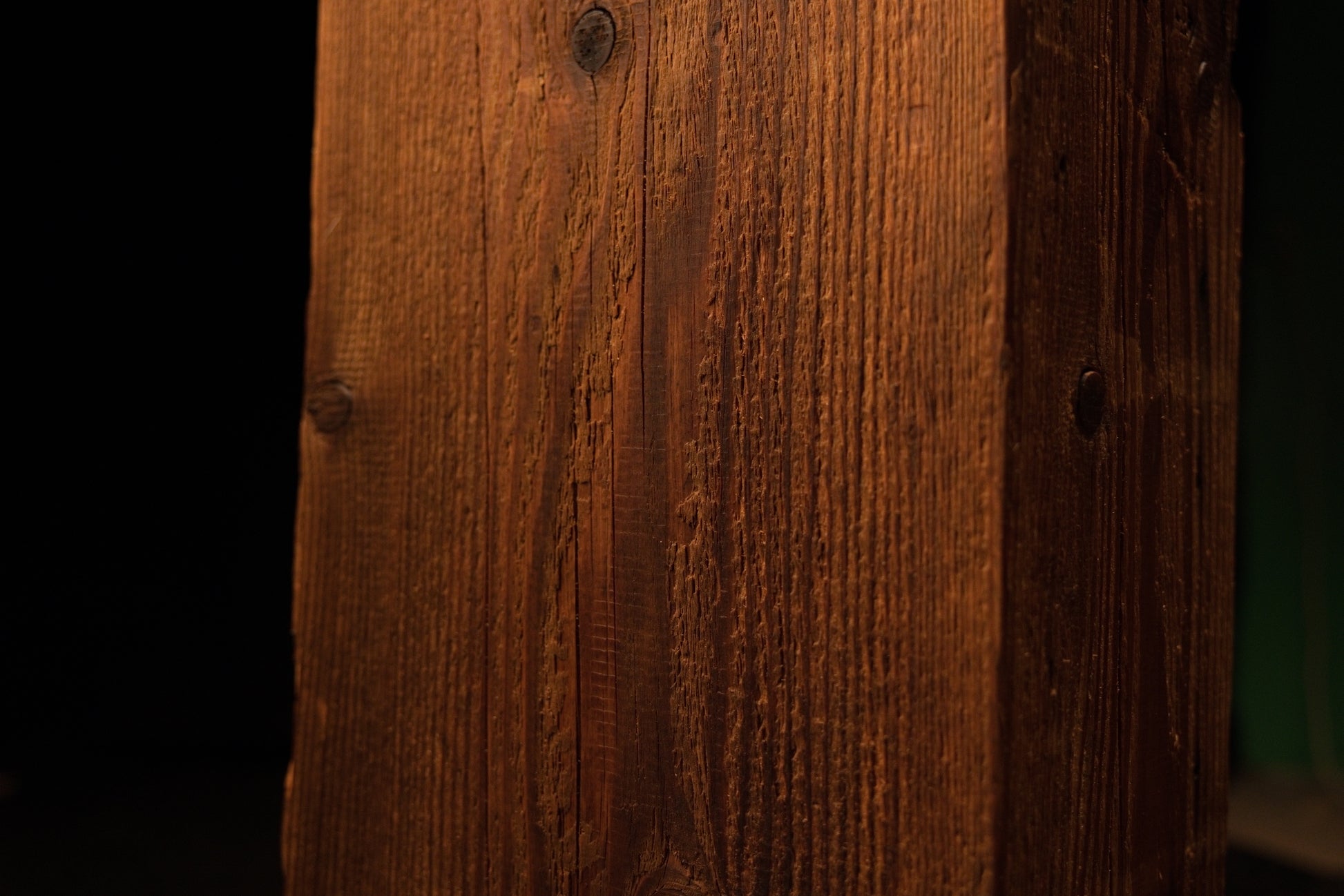 Macro perspective of uniform vertical grain lines and a small dark wood knot on the side of the structural post. 