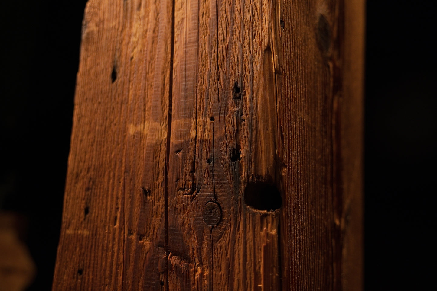 Detailed close-up showing a prominent dark circular hole, pinholes, and vertical splits on the beam surface. 
