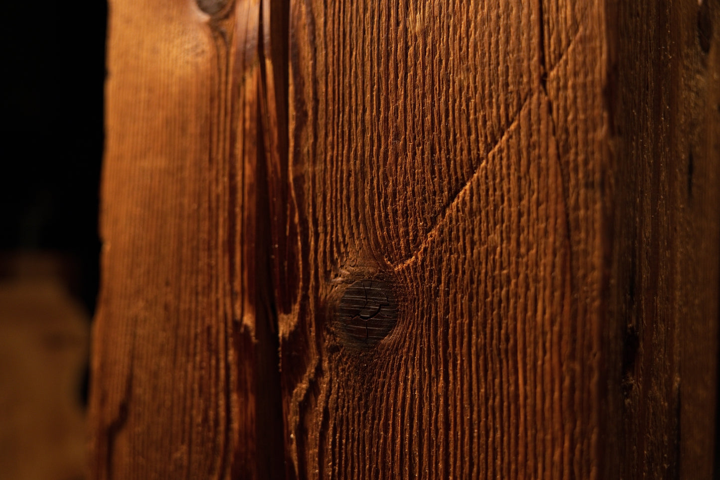 Angled macro perspective highlighting vertical grain lines curving around a dark circular knot on the beam. 