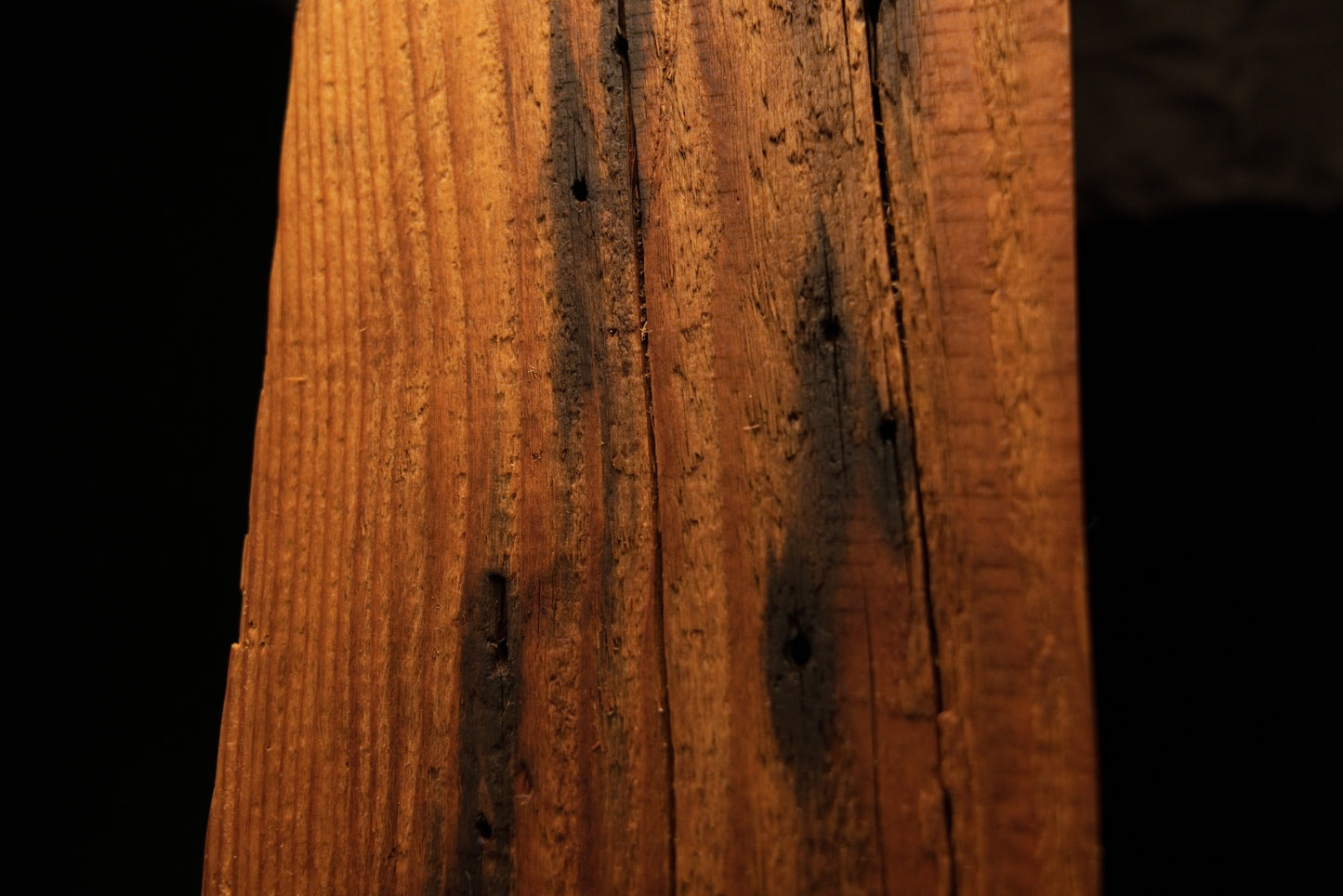 Detailed close-up view of scattered dark pinholes and minor vertical surface fractures along a timber element. 