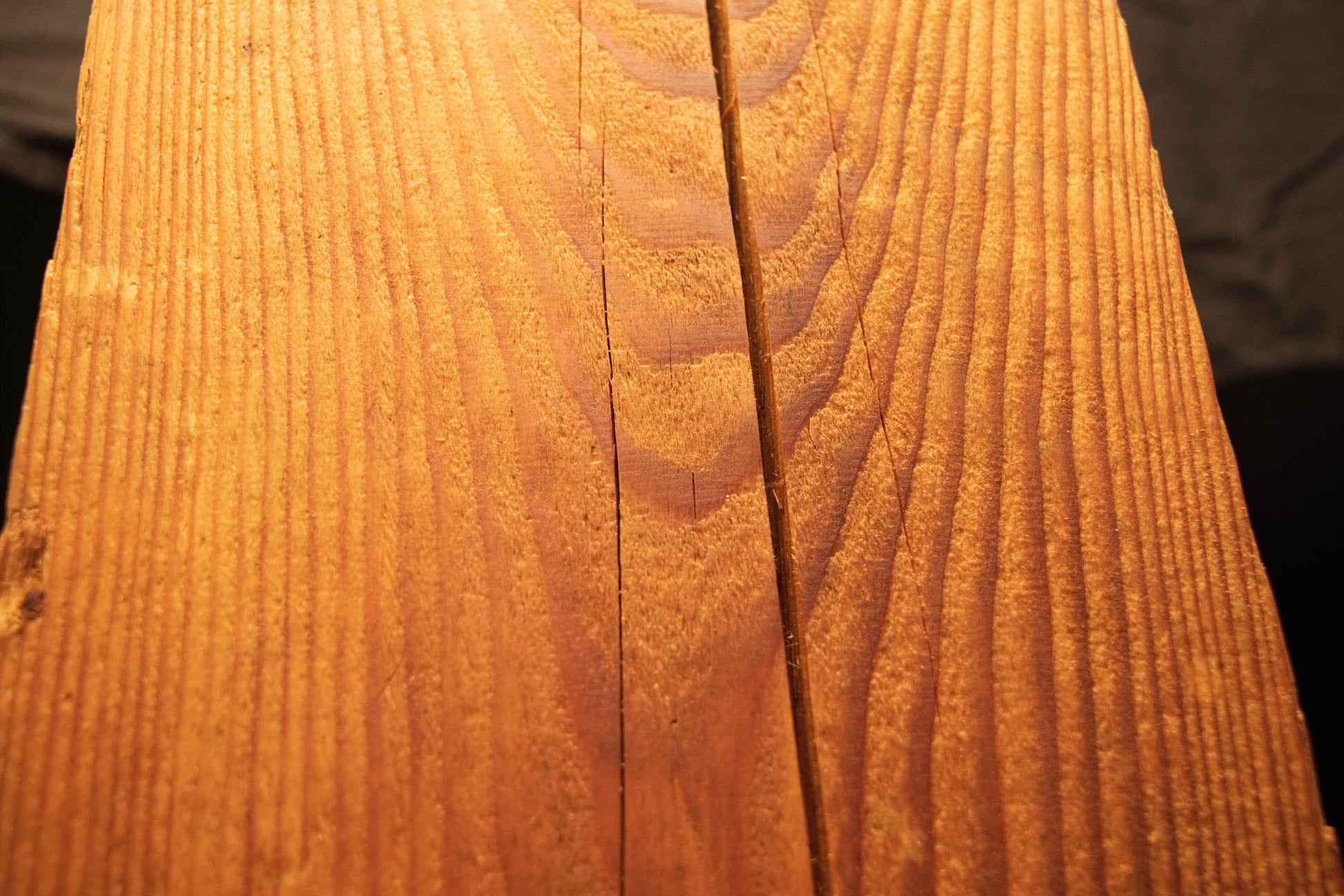 Detailed macro view of a fine central vertical split line running straight through warm amber-toned linear wood grain. 