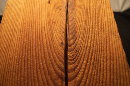 Detailed close-up of rich cathedral grain curves surrounding a vertical surface crack on a structural timber element. 