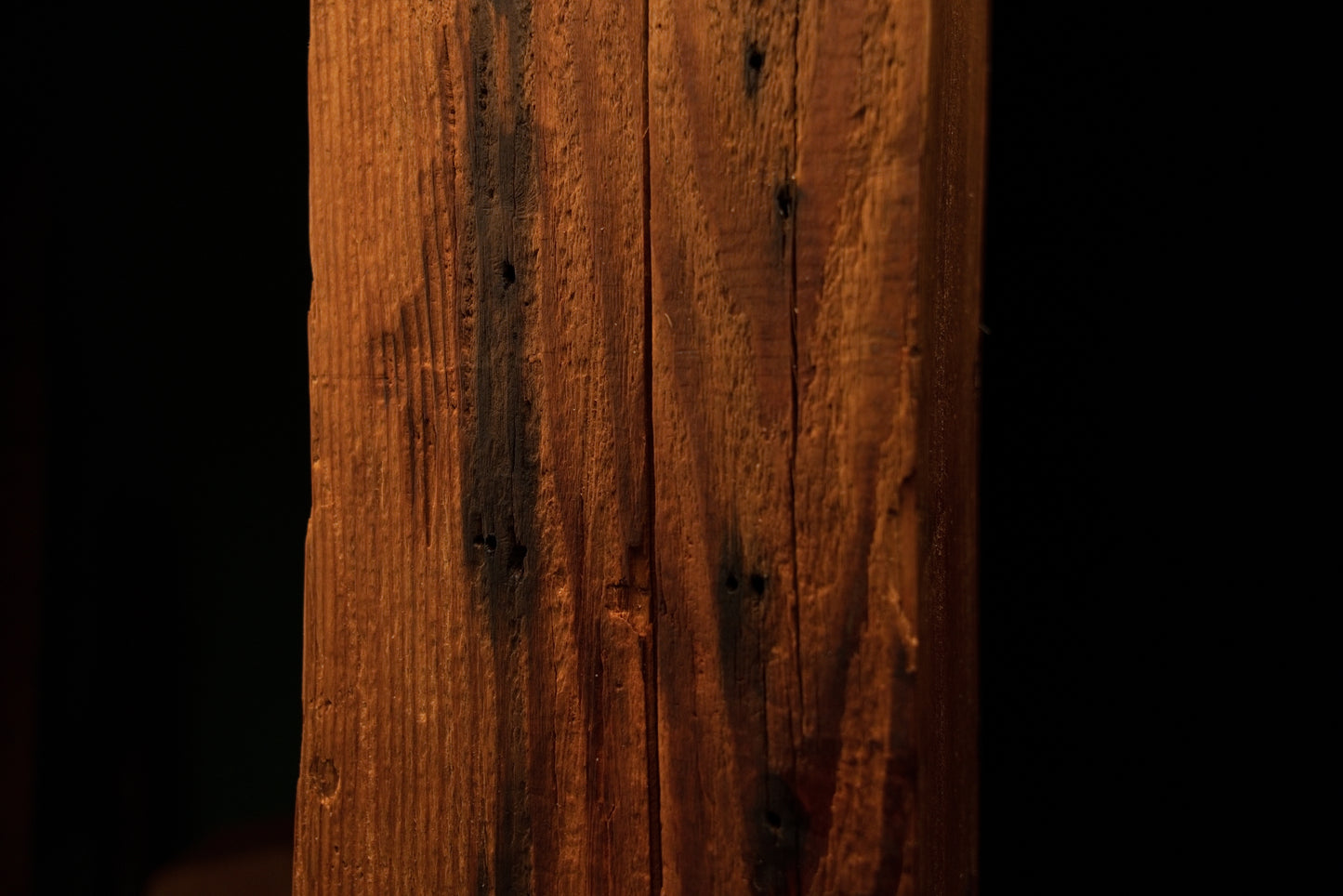 Detailed close-up of a dark oxidation stain stretching alongside a central vertical crack on a wooden beam face. 