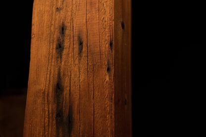 Detailed macro shot highlighting dense vertical wood fibers and scattered dark pinholes on a structural timber post. 