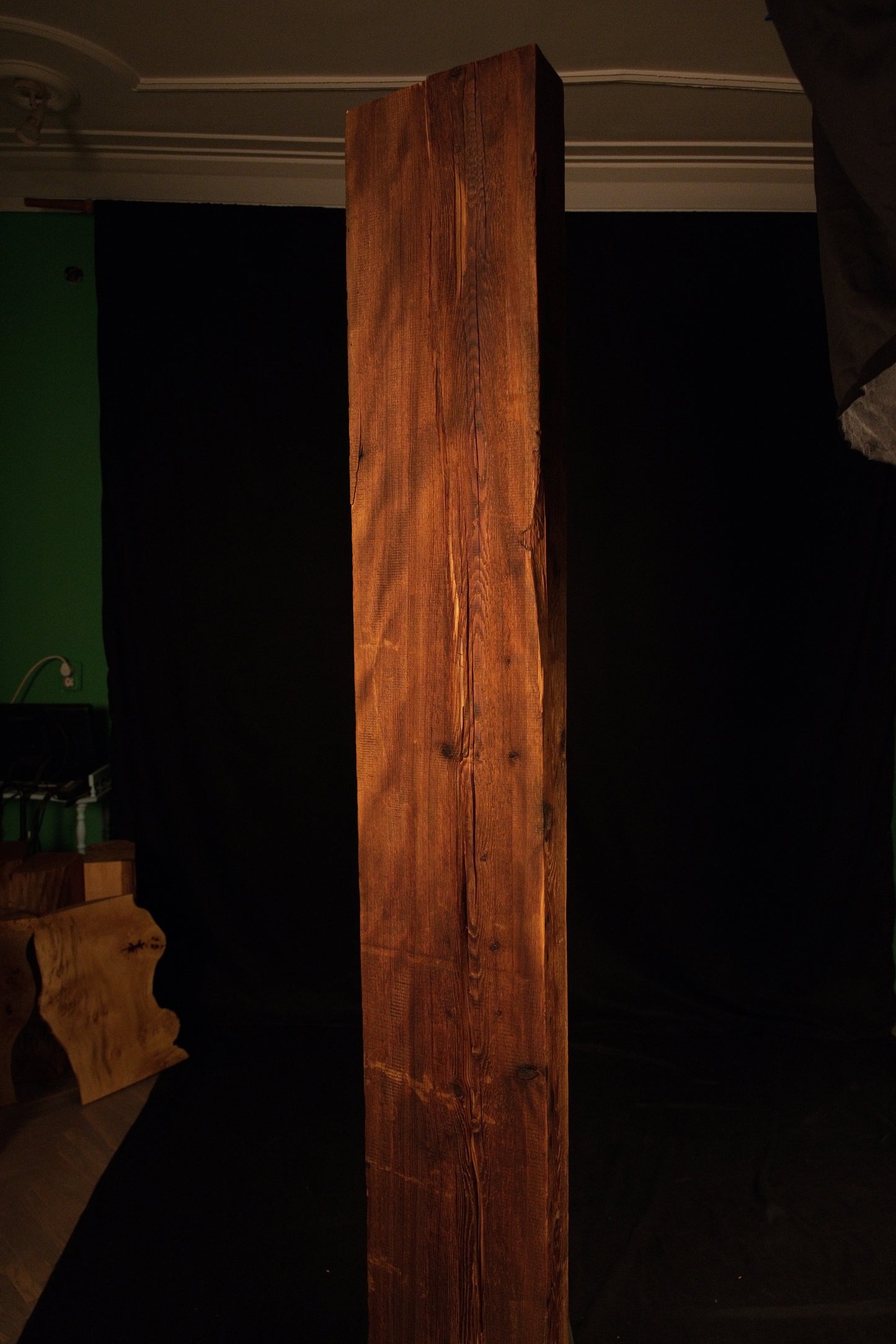 Full standing elevation view of a tall structural timber beam featuring rich amber tones and linear grain against a dark studio. 