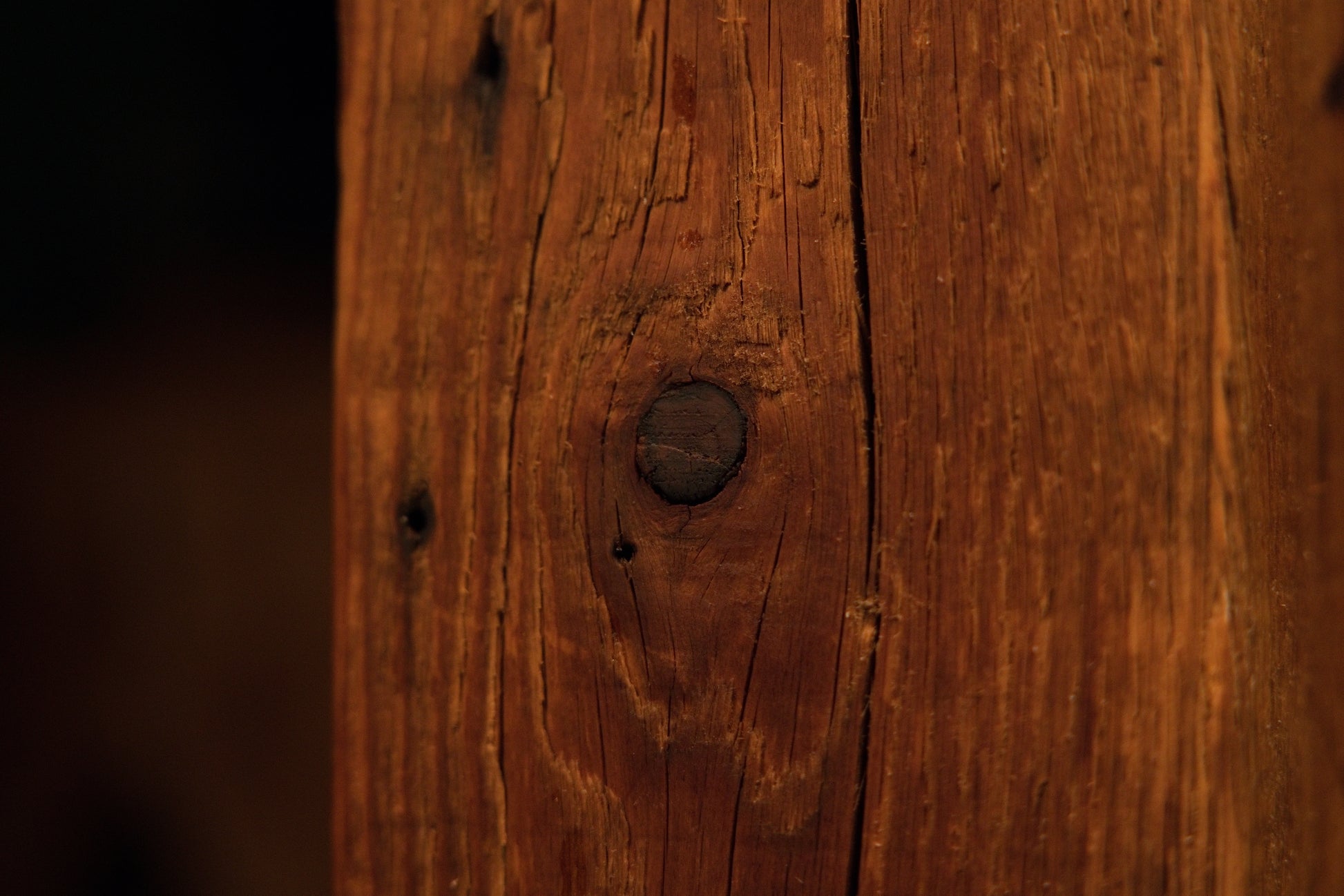 Close-up photograph of a prominent dark circular knot embedded securely within the vertical grain of a solid architectural post. 