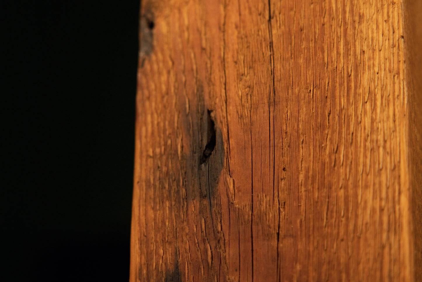Detailed view of a dark oxidation stain patch and small embedded pinholes along the textured face of a heavy wooden column. 