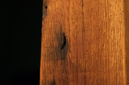 Detailed view of a dark oxidation stain patch and small embedded pinholes along the textured face of a heavy wooden column. 