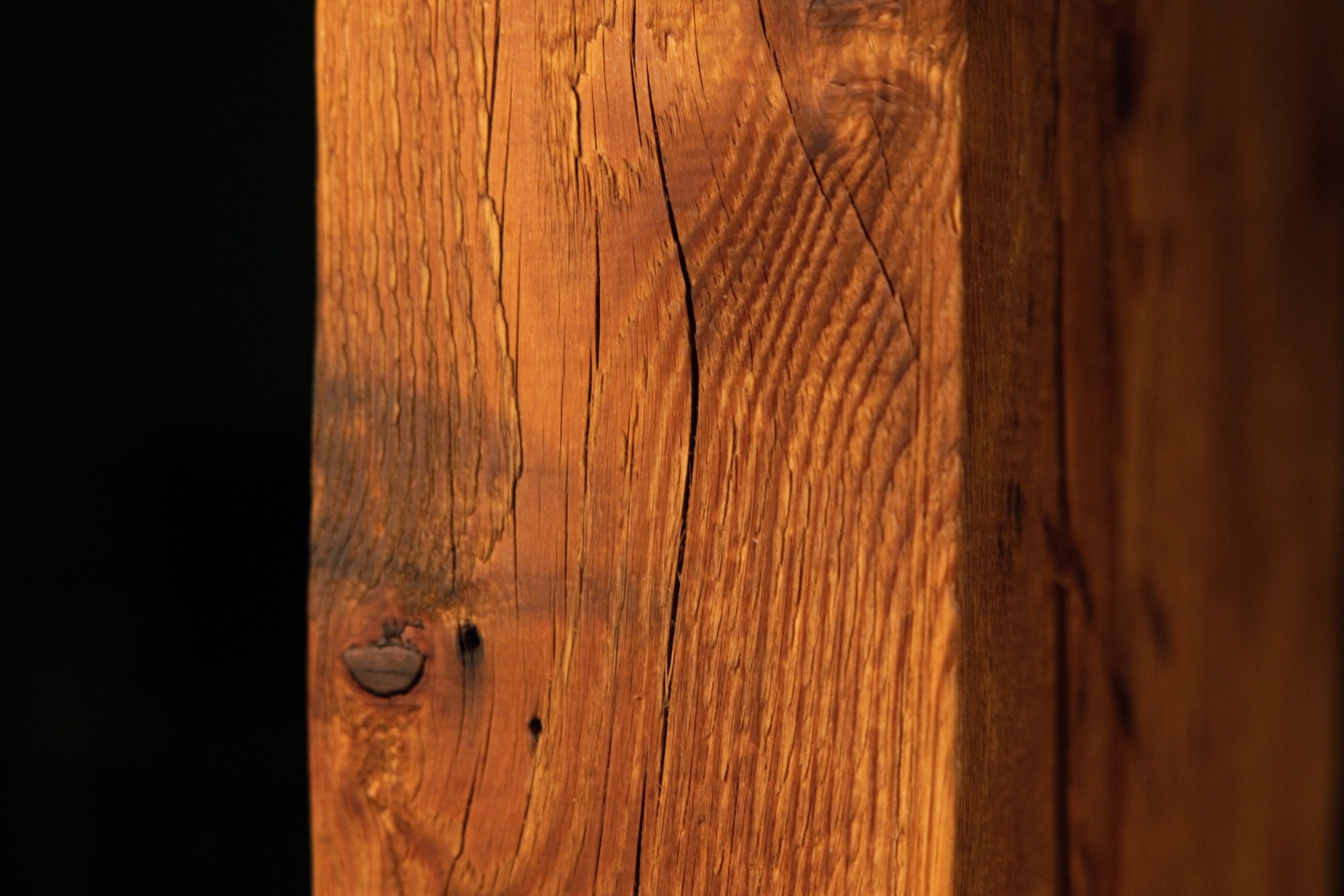 Macro view of a vertical surface crack curving gracefully around a small dark circular knot on a fully stabilized timber. 