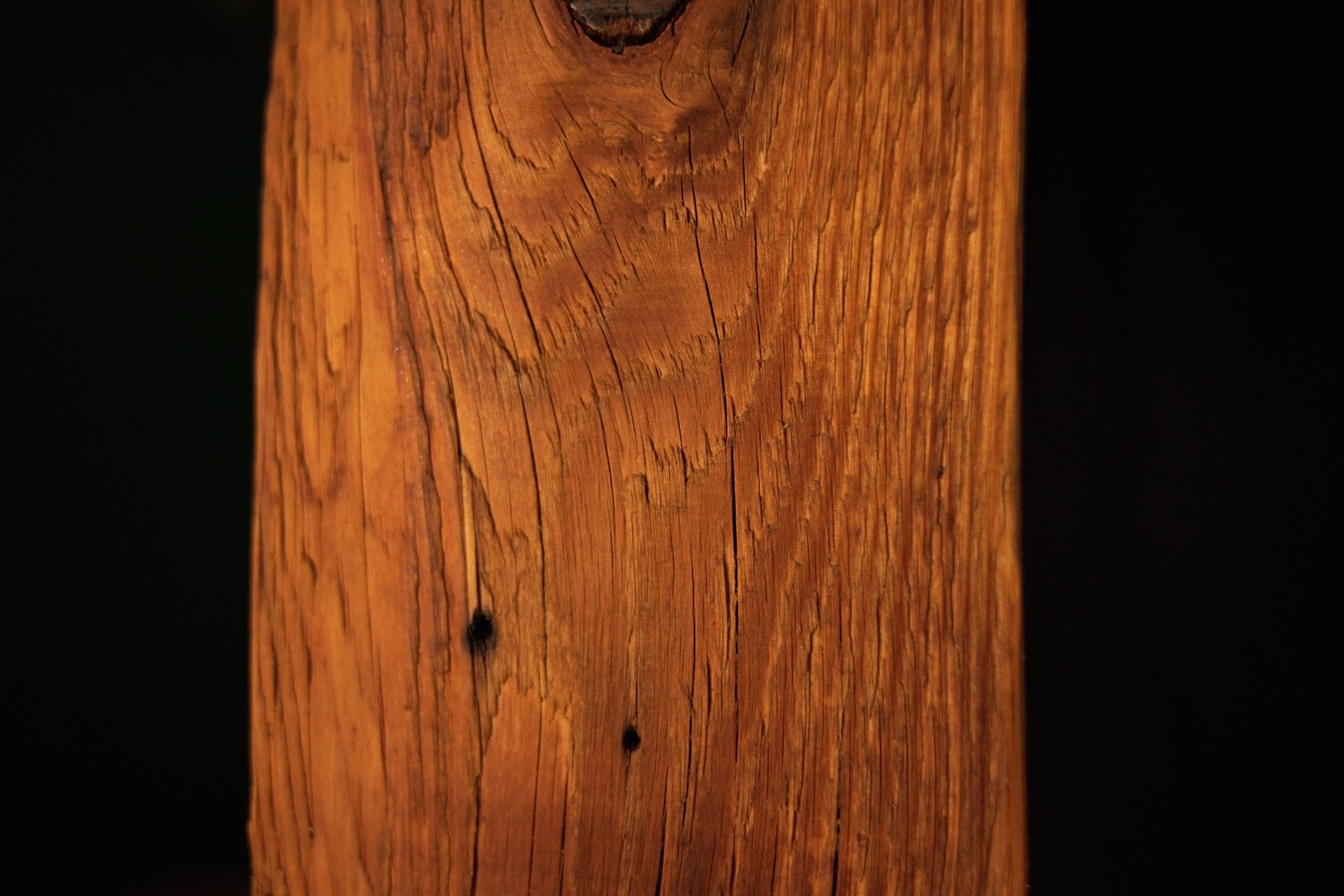Detailed close-up showing two small dark pinholes arranged vertically amidst linear grain patterns on an architectural post. 
