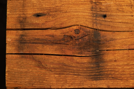 Frontal view of a climate-stable structural timber board featuring a central dark knot and horizontal check lines across the face. 