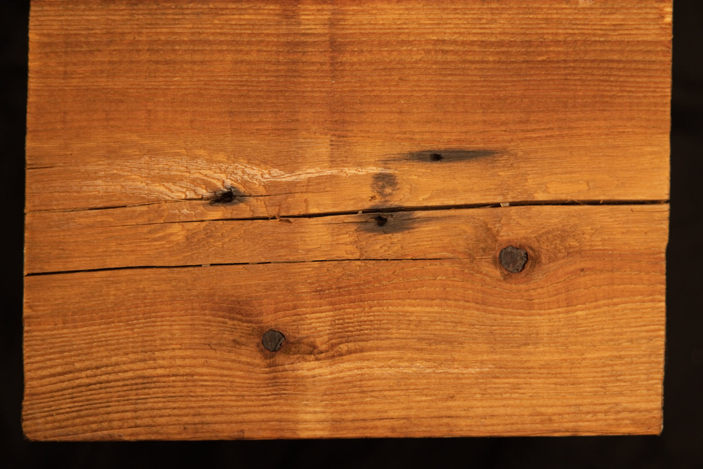 Flat surface view of a floor-heating compatible wooden plank displaying multiple dark organic knots and a horizontal check. 