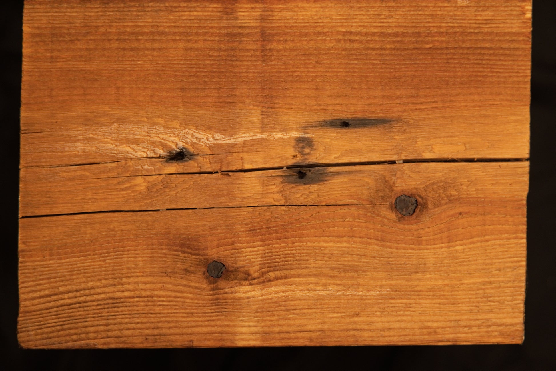 Flat surface view of a floor-heating compatible wooden plank displaying multiple dark organic knots and a horizontal check. 