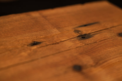 Angled macro close-up of a museum-grade biophilic timber surface highlighting dark knot inclusions and a surface check. 